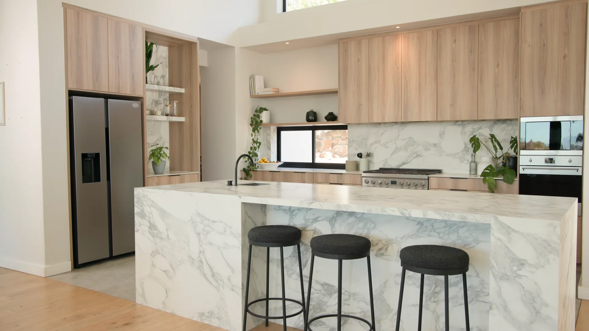 Light stone waterfall island in a warm wood kitchen